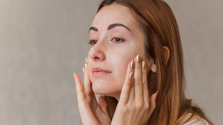 A woman applying a serum or cream to her face in front of a grey backdrop.