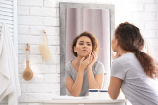 young woman with acne  looking in mirror at home