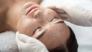 Close up of young woman getting facial skin treatment at spa. Hands applying scrub mask on her face.