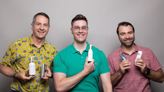 Three men standing in a row holding up skincare products