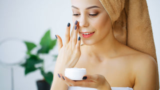 A woman applying face cream with a towel on her head after the shower 