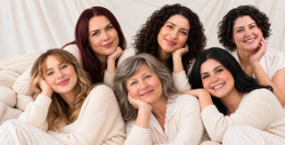 Six women from the Art of Skin Care team smiling and laughing together in a relaxed group portrait, wearing soft neutral outfits.