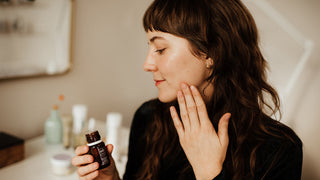 side view of woman holding skincare product and touching cheek