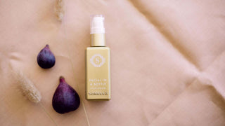 A serum, Facial in a Bottle, that has Azelaic acid sits on a cloth next to some figs.