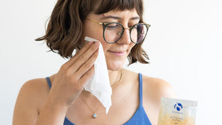 Woman holding an iS Clinical Active Peel System pouch in her hand and swiping a wipe on her cheek.