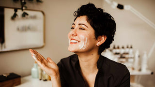 A smiling woman washing her facing with a foaming cleanser