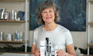 Woman in sliver shirt with skincare products in a row on a table