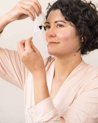 Woman applying a hydrating sheet mask as part of an at-home professional skincare treatment.