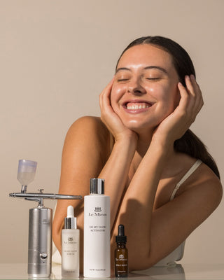Woman with glowing skin beside Le Mieux Ionized Oxygen Infuser and Oh My Glow skincare products for an at-home facial treatment.