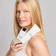Woman holding two Colorescience Total Protection No-Show Mineral Body Shield SPF 50 sunscreen tubes against her shoulder