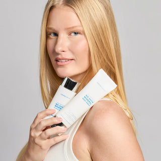 Woman holding two Colorescience Total Protection No-Show Mineral Body Shield SPF 50 sunscreen tubes against her shoulder