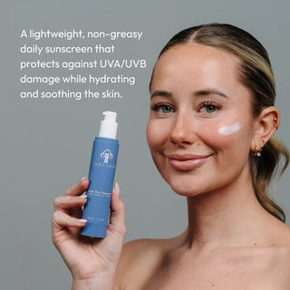Woman holding Circadia Light Day Sunscreen SPF 37 with sunscreen applied to cheek — lightweight non-greasy daily sunscreen that protects against UVA/UVB damage while hydrating and soothing the skin