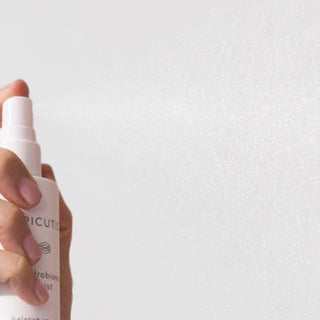 Hand Hand spraying Epicutis Hydrobiome Mist facial mist showing a fine mist dispersing in the air on a light gray background
