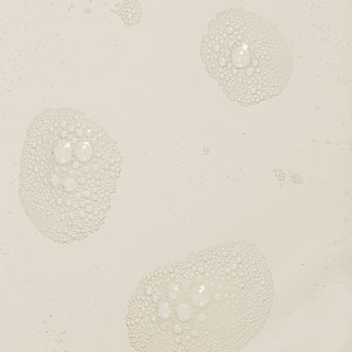Close-up of Rhonda Allison Mandelic Purifying Tonic liquid texture showing clear toner with fine bubble clusters on a warm beige surface
