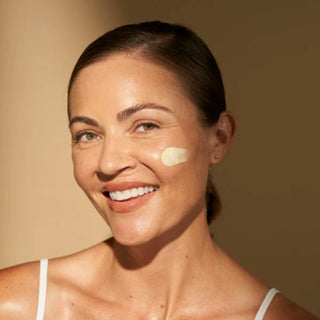 Woman applying ALASTIN A-Luminate Brightening Serum to cheek, smiling in sunlight