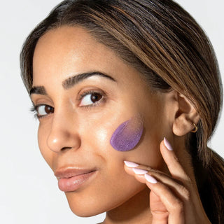 Woman applying purple ALASTIN ReSURFACE Skin Polish exfoliant to cheek