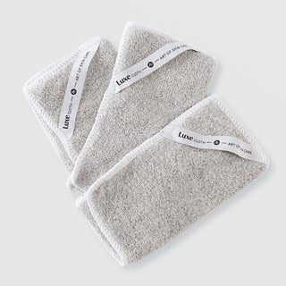 Art of Skin Care Luxe Cloth set of three grey microfibre cleansing cloths with white branded labels, fanned out on white background