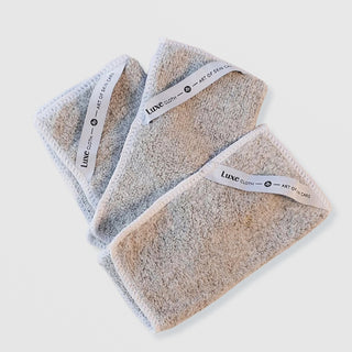 Art of Skin Care Luxe Cloth set of three grey microfibre cleansing cloths with white branded labels, fanned out on white background