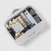 Art of Skincare Signature Cosmetic Case white travel bag with clear front panel filled with assorted skincare products, gold branded label, four compartment organiser