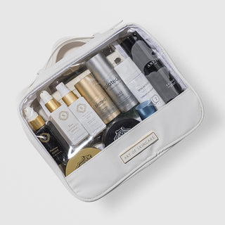 Art of Skincare Signature Cosmetic Case white travel bag with clear front panel filled with assorted skincare products, gold branded label, four compartment organiser