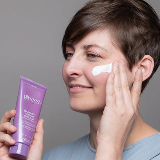 Woman applying GlyMed Plus Elite Barrier Repair Cream with Amino Acids to cheek while holding the purple tube