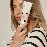A woman with smooth blonde hair holds the SEEN Blow-Out Creme tube alongside her face, with the instruction to apply a dime-to-quarter-size amount to damp hair from roots to ends before blow-drying, heat-styling, or air-drying.