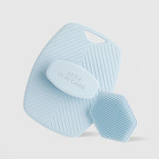 Art of Skin Care large and small blue silicone scrubbies displayed together — the large body scrubby with chevron texture and finger loop alongside the small hexagonal face scrubby with honeycomb bristles, against a light gray background.