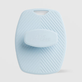 Art of Skin Care large blue silicone body scrubby with chevron texture and a finger loop handle, featuring an embossed Art of Skin Care grip pad, displayed against a light gray background.