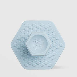 Art of Skin Care small blue silicone face scrubby in a hexagonal shape with honeycomb texture and a raised AS logo grip on the back, displayed against a light gray background.