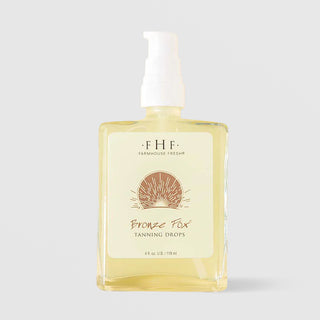 Farmhouse Fresh Bronze Fox Tanning Drops (4 fl oz / 118 ml) in a clear glass pump bottle with a pale yellow formula visible inside, featuring a cream label with a bronze sunburst illustration, displayed against a light gray background.