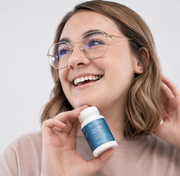 Smiling woman holding Face Reality Clear Skin Restore supplement – daily zinc and probiotic capsule for clearer skin