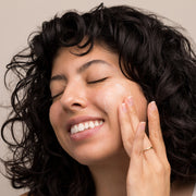 Smiling woman massaging Circadia Lipid Replacing Cleansing Gel onto her face, showing the cleanser's gentle lathering texture on skin
