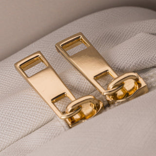 Close-up of Art of Skincare Signature Cosmetic Case gold zip pulls against white textured fabric