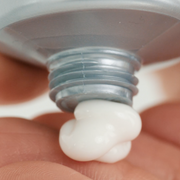 Close-up of iS Clinical Sheald Recovery Balm rich white cream dispensing from silver tube onto fingertip