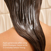 Back view of a person with long dark hair applying SEEN Conditioner in the shower, with white conditioner visible throughout wet hair and the instruction to leave on for 2–3 minutes before rinsing