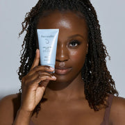 Woman with deep skin tone holding Face Reality Daily SPF 30 Plus – broad-spectrum acne-safe daily sunscreen for all skin tones