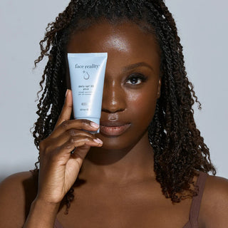 Woman with deep skin tone holding Face Reality Daily SPF 30 Plus – broad-spectrum acne-safe daily sunscreen for all skin tones