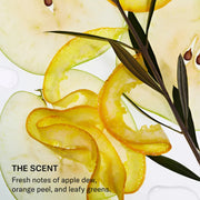 Close-up of thinly sliced green apple, citrus peel curls, and dark leafy stems on a white background, illustrating SEEN Deeper Conditioner's scent notes of apple dew, orange peel, and leafy greens