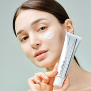 Woman holding Dermathod Ami-Sterol Cream tube with cream swatch applied to cheek, anti-wrinkle brightening facial moisturizer