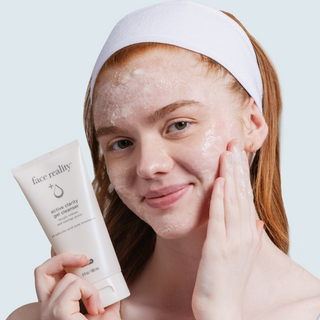 Woman with foamy lather on face holding Face Reality Active Clarity Gel Cleanser tube