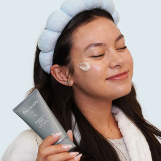 Smiling woman applying Face Reality Brighten-C Mask to cheek – vitamin C radiance mask for acne-prone skin