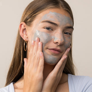Woman applying Face Reality Soothing Clay Mask to face – purifying gray clay mask for acne-prone and oily skin