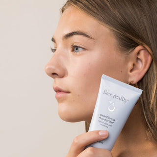 Woman with clear skin holding Face Reality clearDerma Moisturizer – lightweight soothing acne-safe moisturizer for acne-prone skin