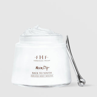 Farmhouse Fresh Moon Dip Back to Youth Ageless Body Mousse in an open white glass jar overflowing with whipped white mousse, displayed alongside a silver spatula against a light gray background.