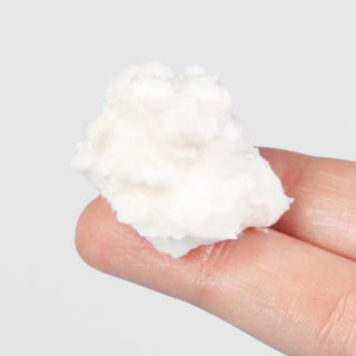 Close-up of a fingertip holding a dollop of Farmhouse Fresh Moon Dip Back to Youth Ageless Body Mousse, showing its light and airy whipped texture against a light gray background.