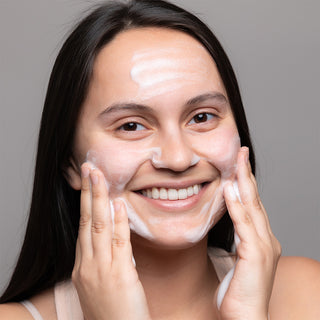 Smiling woman massaging GlyMed Plus Elite Foaming Cleanser with Amino Acids onto face with both hands
