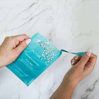 Hands opening FactorFive Growth Factor Post Treatment Facial Mask pouch on marble counter
