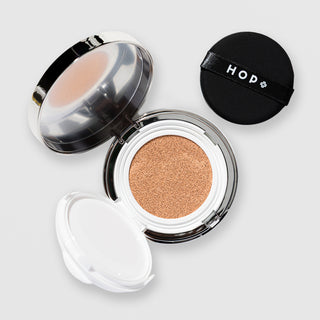 HOP+ Volume Shield Cushion open showing beige foundation-soaked cushion sponge, removable inner tray, black branded puff and mirrored lid, silver compact