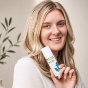 Smiling blonde woman holding Hale & Hush Rare C Serum tube, radiance and pore refinement vitamin C serum for sensitive skin