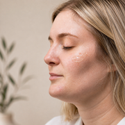 Side profile of blonde woman with eyes closed and a drop of Hale & Hush Rare C Serum applied to cheek, showing lightweight clear formula on sensitive skin